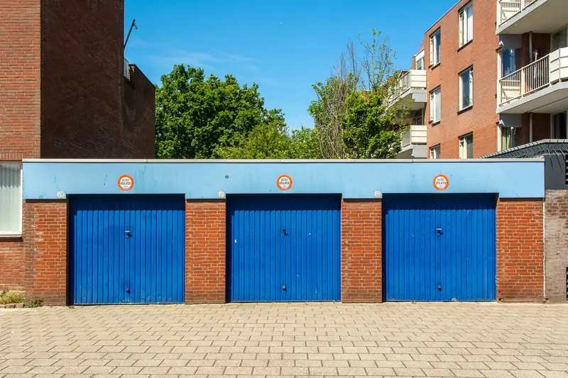 Three blue garage doors in a brick building on a sunny day