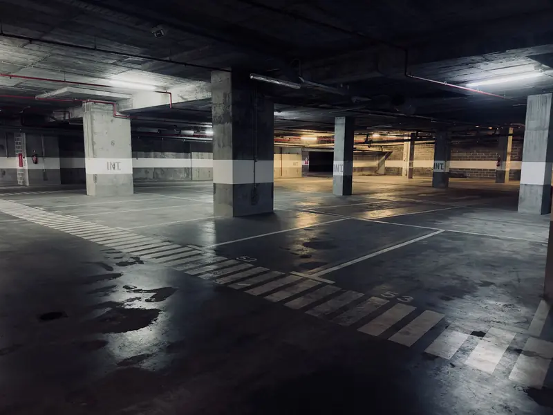 A moody underground parking garage featuring empty spaces and puddles on the floor