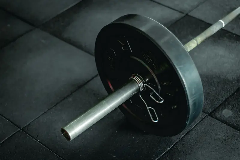 Detailed view of a barbell with heavy weights resting on a dark gym floor mat
