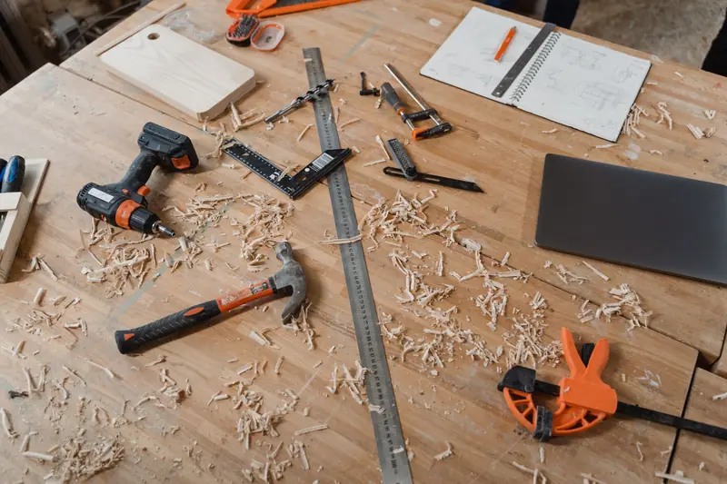 A workbench with various woodworking tools alongside sketches and wood shavings, indicating an active project