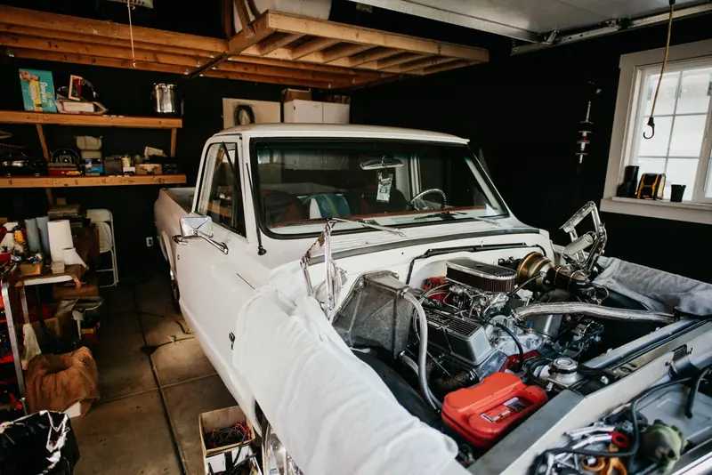 A vintage pickup truck undergoing engine repairs in a well-equipped home garage