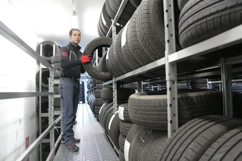 Mechanic places a tire on a rack in an indoor warehouse storage facility