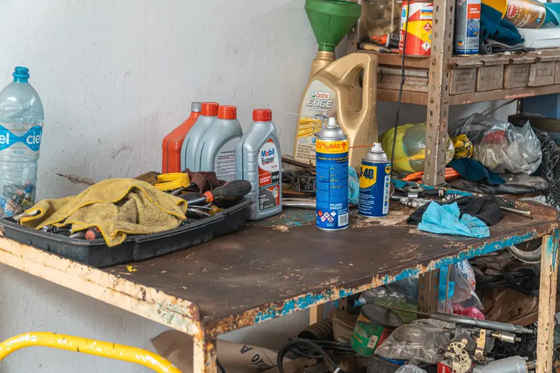 A cluttered workbench in an automobile garage with tools, oil cans, and maintenance products