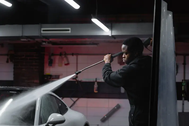 A man uses a high-pressure hose to wash a car in an indoor garage setting