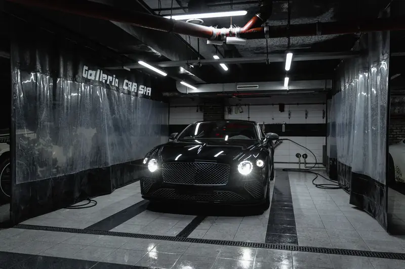Sleek black car with headlights on, parked in a stylish garage with bright lighting
