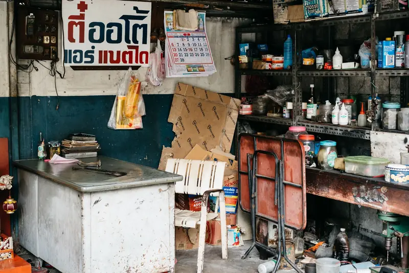 A cluttered garage workshop with various tools, shelves, a desk, and visible clutter